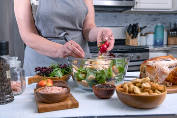 Cook adds cherry tomatoes to glass bowl with salad in home kitchen.Cooking Caesar salad.