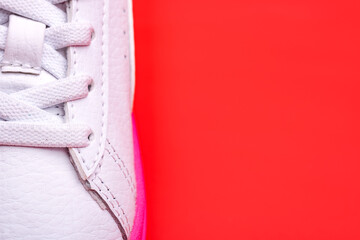 Laced fastening of new sports shoe close-up. Elastic laces of modern textile trainers for active lifestyle, sport, and fitness on red background. Copy space.
