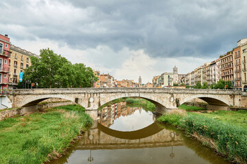 Colorful yellow and orange houses and bridge Pont de Sant Agusti reflected in water river Onyar, in Girona, Catalonia, Spain. Church of Sant Feliu and Saint Mary Cathedral at background. BRIDGE in the