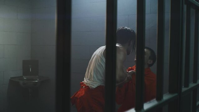 Male prisoners quarrel and fight in prison cell. Criminal presses cellmate against metal bars, yells, talks aggressively. Inmates in orange uniforms in jail, detention center or correctional facility.