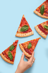 Woman taking slice of tasty pizza on blue background