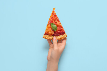 Woman holding slice of tasty pizza on blue background