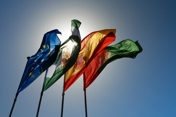 Spanish, Portuguese and European Union flags hoisted in flagpoles with crosses in clear blue sky