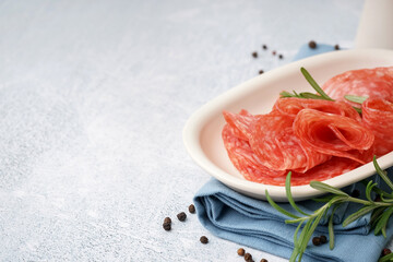 Bowl with slices of tasty salami on light background