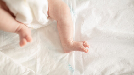 The little legs and feet of a newborn baby in a diaper, in the crib, at home