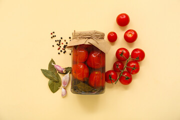 Jar with canned tomatoes and garlic on beige background