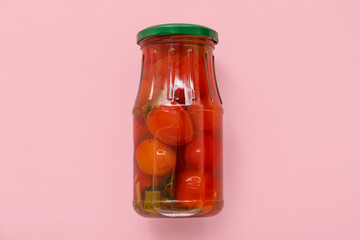 Jar with canned tomatoes on pink background