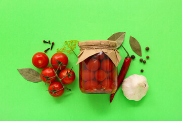 Jar with canned tomatoes, peppercorn and garlic on green background