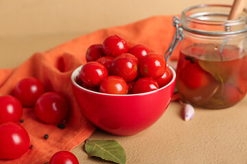 Bowl and jar with canned tomatoes on brown background