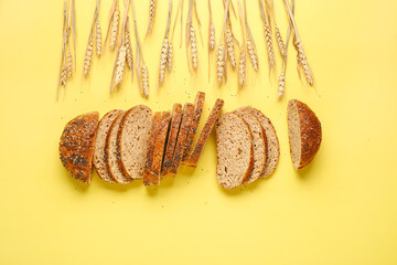 Loaf of sliced rye bread and wheat ears on yellow background