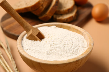 Fototapeta na wymiar Bowl with wheat flour and scoop on beige background, closeup