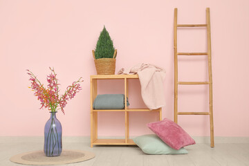 Shelving unit with cozy blankets, cushions and houseplant near pink wall