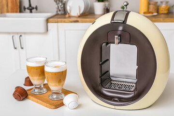 Modern coffee machine with glasses of hot latte on table in kitchen
