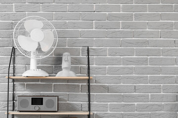 Shelf with electric fan and decor hanging on grey brick wall in room