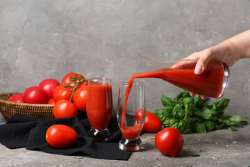 Woman pouring tasty tomato juice from jug into glasses on grey background