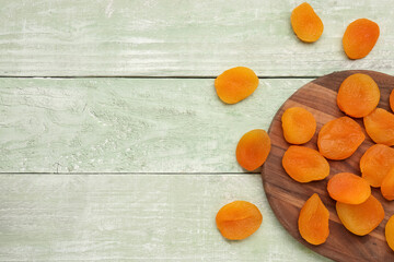 Board with tasty dried apricots on green wooden background