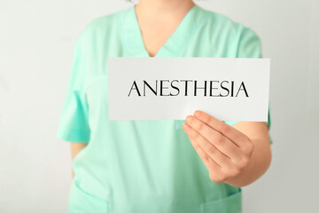 Female doctor holding paper with word ANESTHESIA on light background, closeup