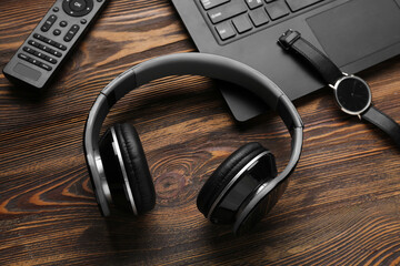 Modern headphones, wristwatch and remote controller on wooden background, closeup
