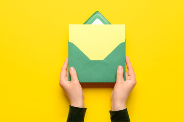 Female hands with envelope and blank card on yellow background, closeup