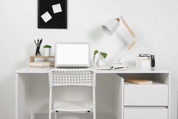 Cozy workspace with laptop, lamp and stationery on wooden desk at home