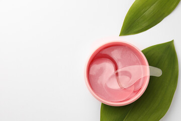 Jar of under eye patches with spoon and green leaves on white background, top view with space for text. Cosmetic product
