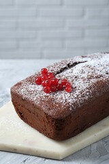 Tasty chocolate sponge cake with powdered sugar and currant on light grey textured table, closeup