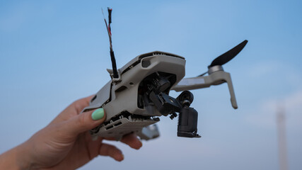 Woman holding crashed drone against blue sky. 