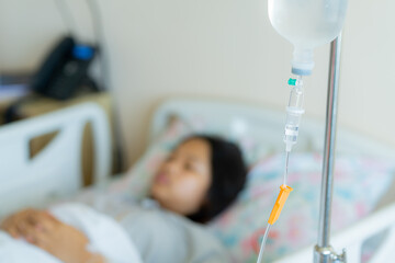 Young patient asian woman lying on the bed in hospital with IV saline drip to the back of the hand, teenager sick in hospital, Selective focus, healthcare, and health insurance concept.