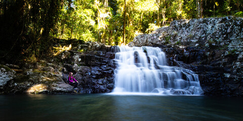 A beautiful girl sits in front of a stunning, powerful waterfall; hike in Gondwana Rainforest on...