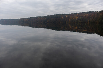 Fototapeta premium Green and orange trees surrounding a lake in autumn and reflecting in the water. 
