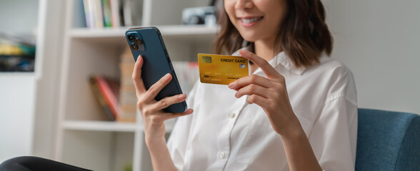 Happy young Asian woman holding credit card and using smartphone for shopping online with payment...