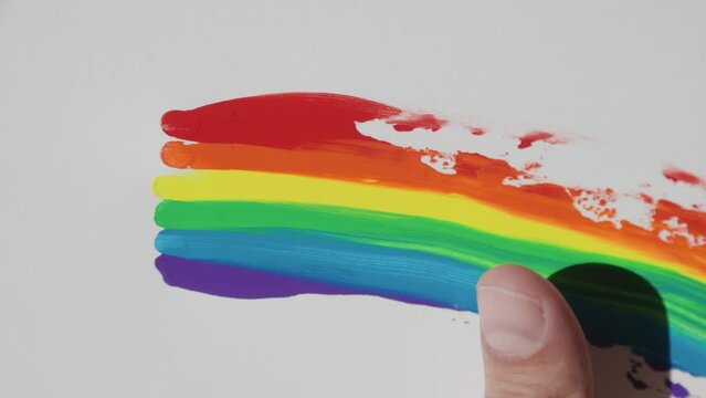 LGBT design, rainbow flag, Close-up of a man's hand smearing drops of acrylic paints on a white sheet of paper. lesbian, gay, bisexual, transgender social movements. Rainbow. Artistic watercolor