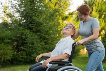 A caucasian woman is carrying an elderly mother sitting in a wheelchair through the park. Walk...