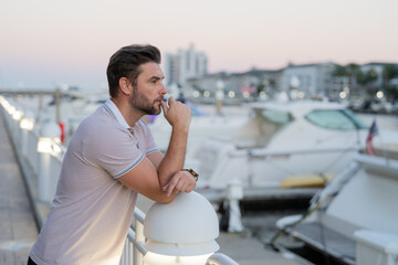 Rich businessman dreaming and thinking near the yacht. Portrait of stylish male model outdoor. Fashion male posing near skyscraper on the street. Fashionable man in urban style.