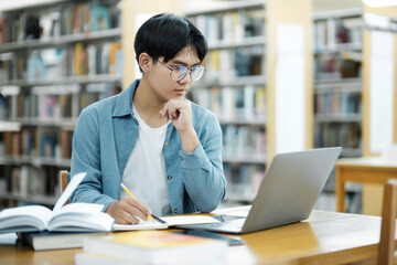 Young university student using laptop for online learning, searching and learning at library.