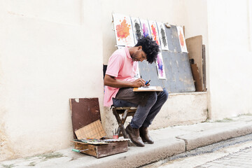 african american man artist or painter in the street painting on footpath in Latin America, Afro...