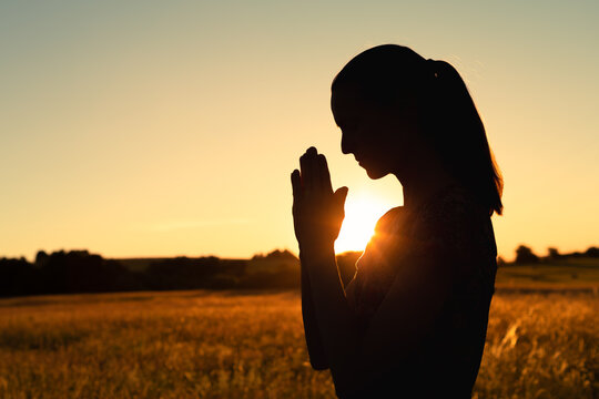 Silhouette of young woman saying a prayer outdoors in the sunlight 