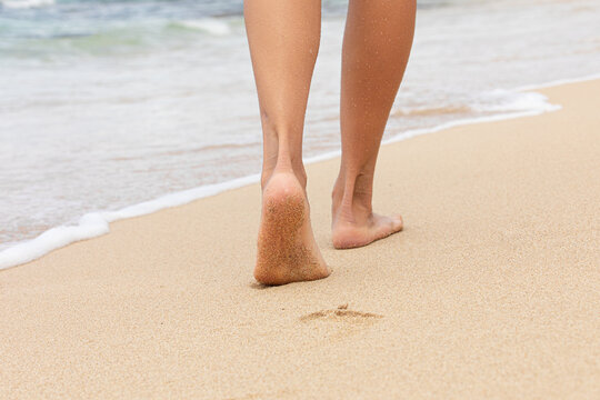Barefoot person walking on sandy beach near the sea during vacation.