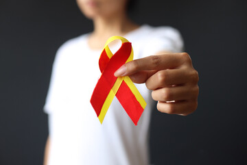 World hepatitis day. Woman holding red yellow ribbon and showing it to camera. Awareness of prevention and treatment viral hepatitis. Liver cancer. Selective focus. Close-up