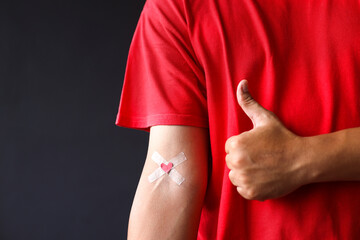 Man showing thumbs up near hand with plasters heart after giving blood. World Blood Donor Day, World Hemophilia Day concept.