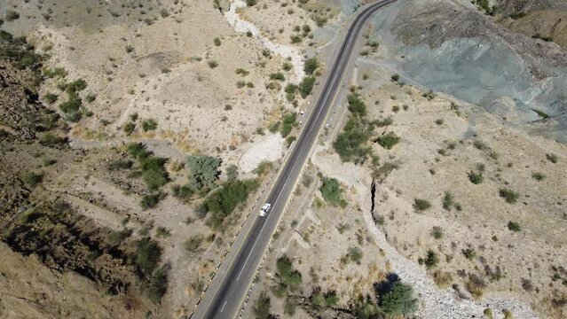 Aerial drone view of car driving down desert highway in rocky mountain landscape in Balochistan