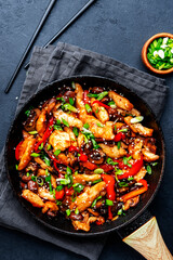Asian cuisine stir fried chicken, paprika, mushrooms, chives with sesame seeds in frying pan. Black kitchen table background, top view