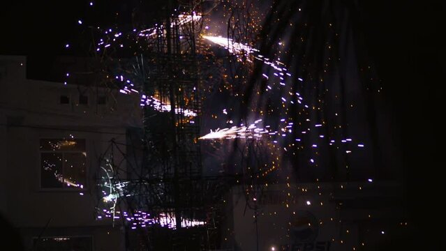 Low angle shot of celebrations underway in a distance of burning effigy with crackers at night time.