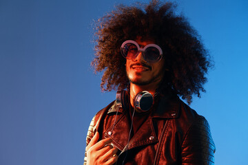 Portrait of a stylish man with curly hair with glasses and headphones on a blue background...
