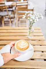 Man wrists tied with an elastic bandage. Cup of hot cappuccino. The table in the coworking space of the coffee shop. A cup of coffee on the veranda on a sunny day. Coffee break at the cafe. Close-up