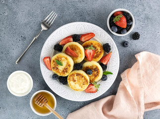Cottage cheese pancakes, syrniki with sour cream, honey, berries on blue background. Top view. Russian, ukrainian food