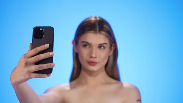 Rack focus selfie posing young woman to smartphone, isolated blue background