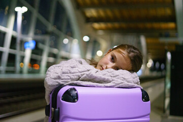 Little charming girl tourist is waiting for train at station in evening