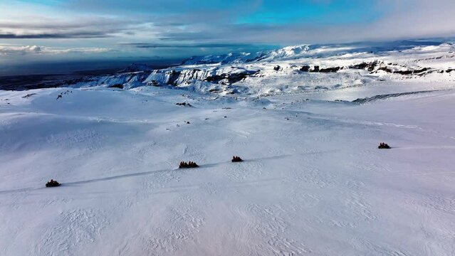Aerial panoramic landscape view of people riding snowmobiles on Myrdalsjokull glacier in Iceland, at dusk