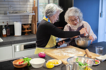 タブレットでレシピを参考にしながら一緒に料理をするシニア女性たち